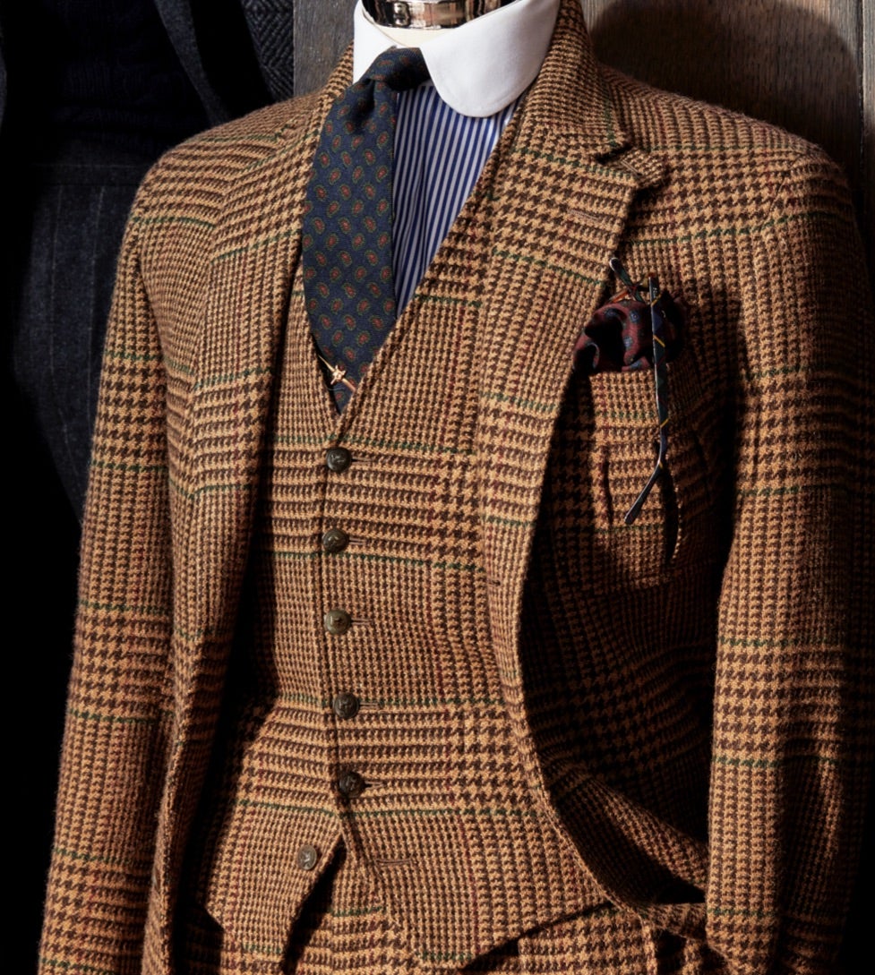 <strong>LES CARREAUX</strong><br/><span>Un costume trois-pi&egrave;ces &agrave; motif prince-de-galles oversize cognac et camel. Le tissu a non seulement &eacute;t&eacute; tiss&eacute; exclusivement en Grande-Bretagne pour la collection ; mais il arbore aussi un motif typiquement Polo : les carreaux-fen&ecirc;tre lie-de-vin et vert permettent de &laquo; retenir &raquo; le motif et les couleurs bordent l'&eacute;cossais, ce qui conf&egrave;re au mod&egrave;le un style Ralph Lauren iconique</span>
