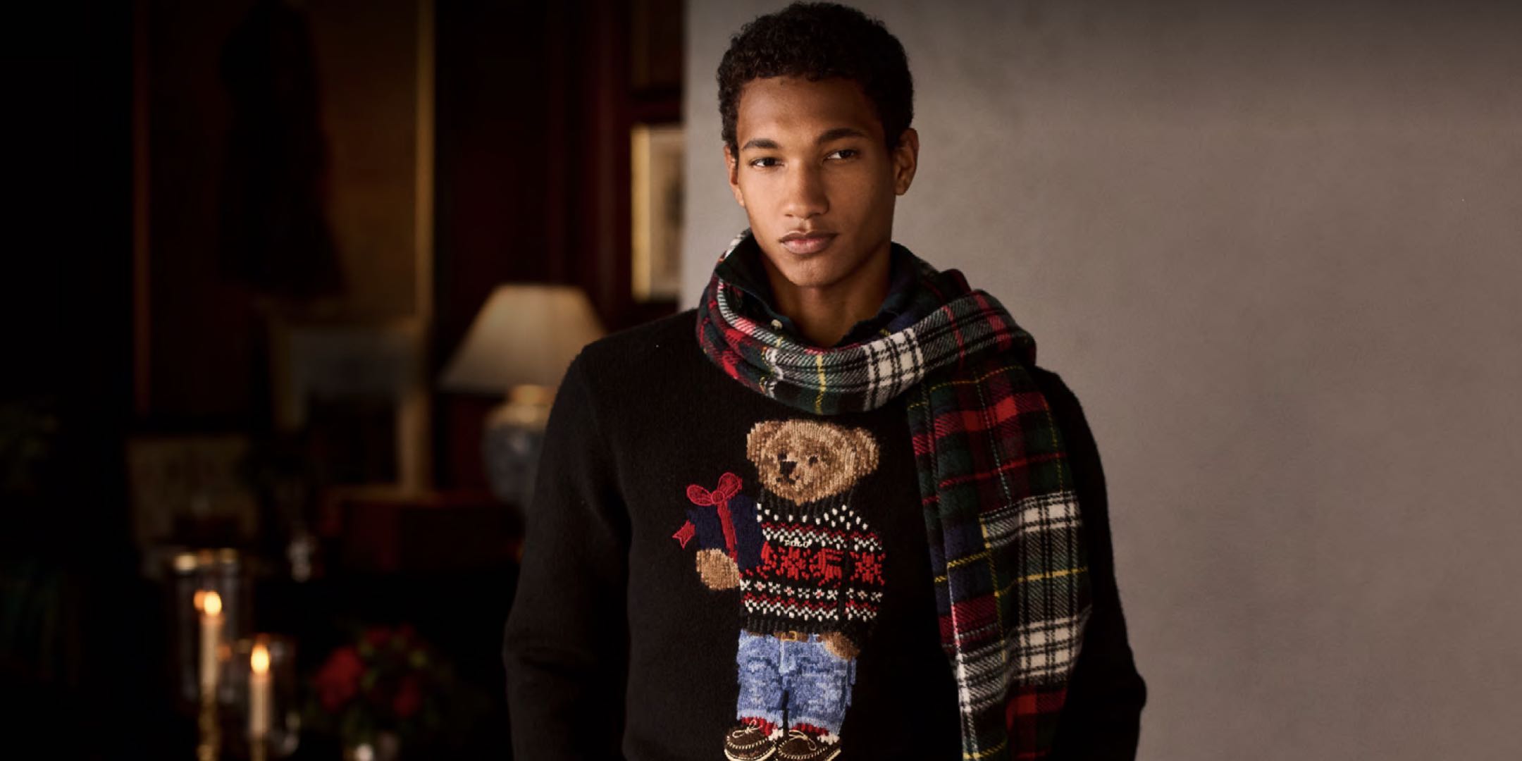Man wears black sweater with Polo Bear at front and a plaid scarf.