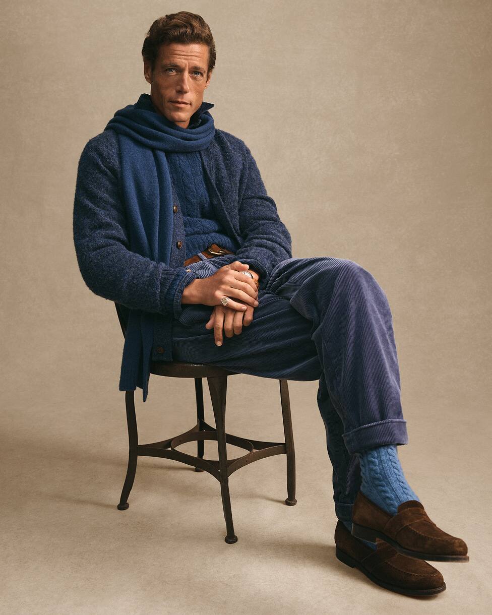 Homme assis portant un tricot bleu et une écharpe assortie avec des mocassins marron.