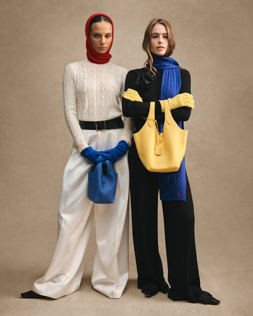 Deux femmes debout, l'une vêtue d'un tricot crème avec une écharpe rouge et des gants bleus, l'autre vêtue d'un tricot noir avec une écharpe bleue et un sac jaune.