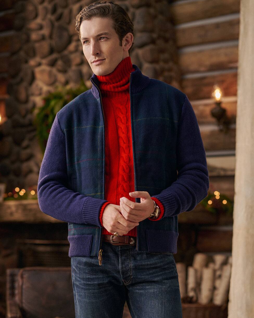 Homme portant un pull col roulé torsadé rouge, une veste marine et un jean.